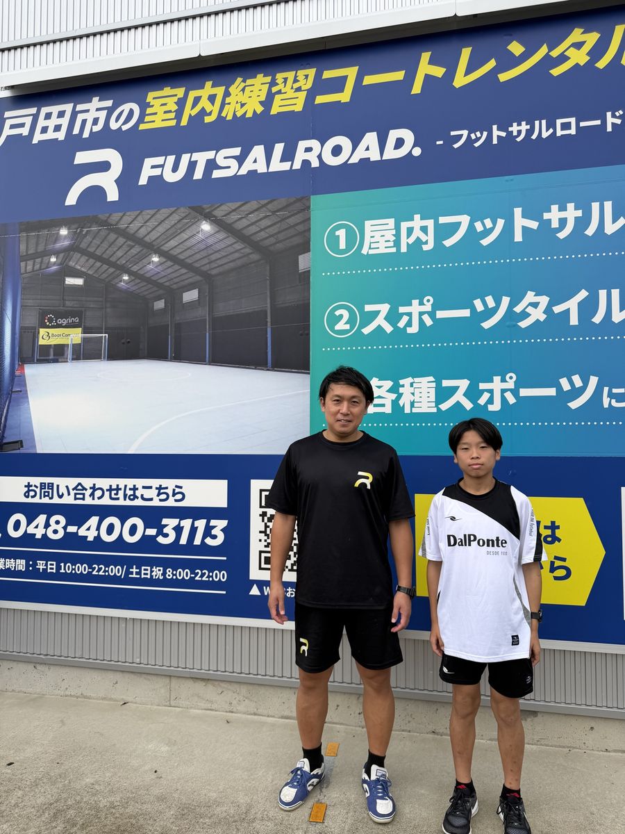 フットサルロードの外壁の看板の前に並ぶスタッフとWataru